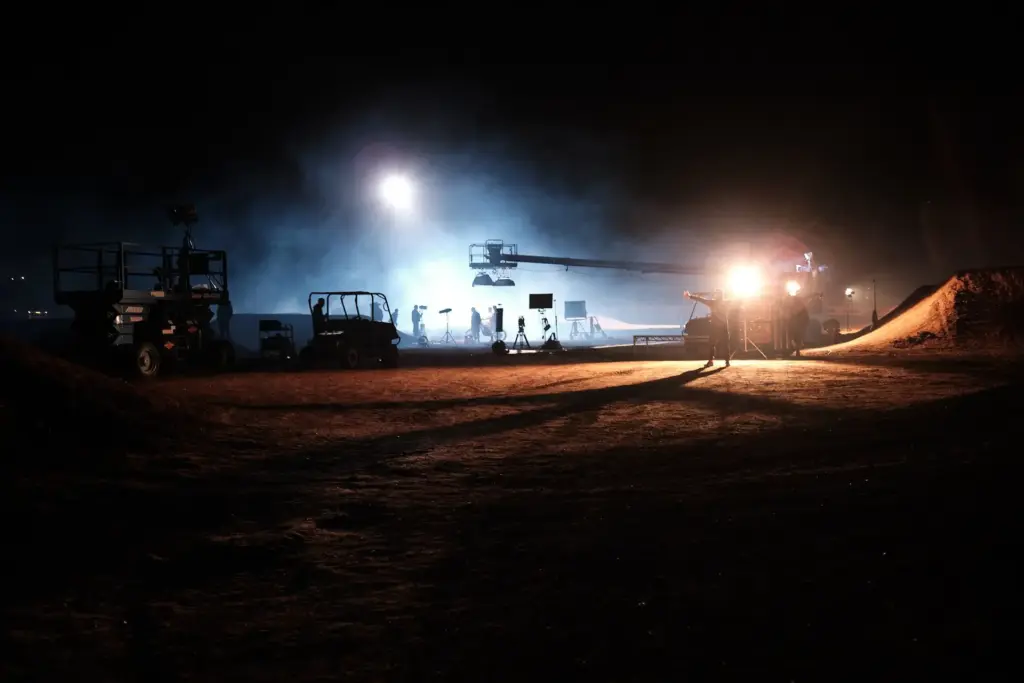 Nachtdreh in der Wüste: Kamerakran, Scheinwerfer und Fahrzeuge der Crew im Nebel unter dunklem Himmel.