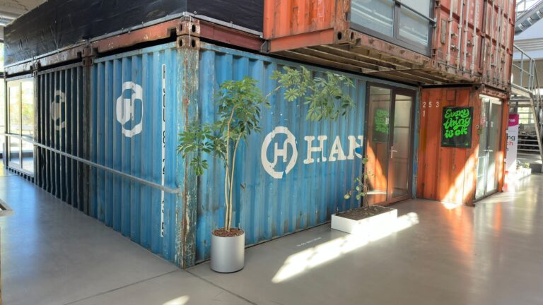 Container im Perfekt Futur in Karlsruhe: Zwei gestapelte Schiffscontainer in Blau und Rostorange mit Glastür und Pflanzen in einer Halle.